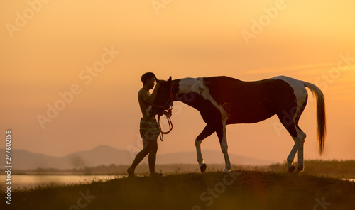 Young man with a horse at the lakeside during sunset