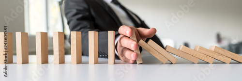 Business mediator stopping falling wooden dominos with his hand