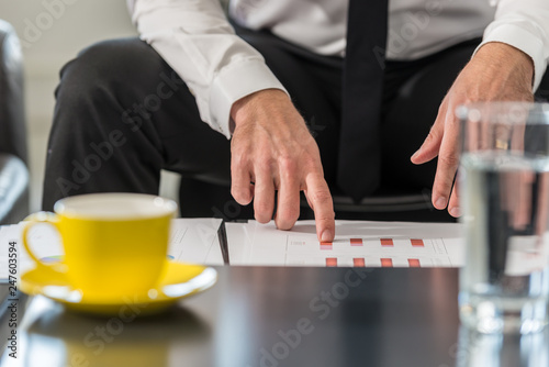 Businessman sitting at a club table in his office reviewing statistical charts