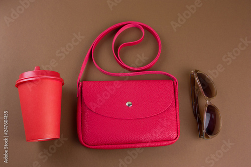 top view female bag, sun glasses and take away drink cup on brown background