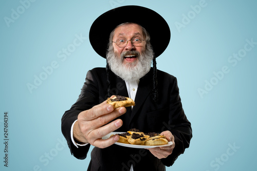 The senior orthodox Jewish man with black hat with Hamantaschen cookies for Jewish festival of Purim at studio. The purim, jewish, festival, holiday, celebration, judaism, pastry, tradition, cookie photo