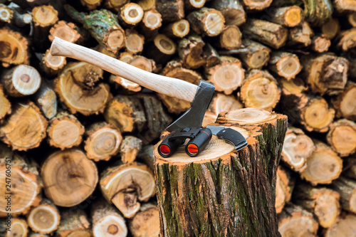 axe, binoculars and jackknife case on the stump, firewoods on the background photo