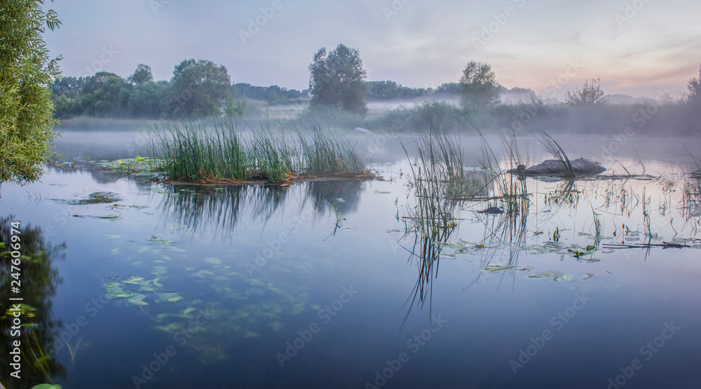Foggy summer landscape with small forest river. Summerall hazy evening.Twilight.Calm stream of river flowing between the woods and meadows covered by fog.Colorful clouds in sky at sunset Foggy summer landscape with small forest river. Summerall hazy evening.Twilight.Calm stream of river flowing between the woods and meadows covered by fog.Colorful clouds in sky at sunset