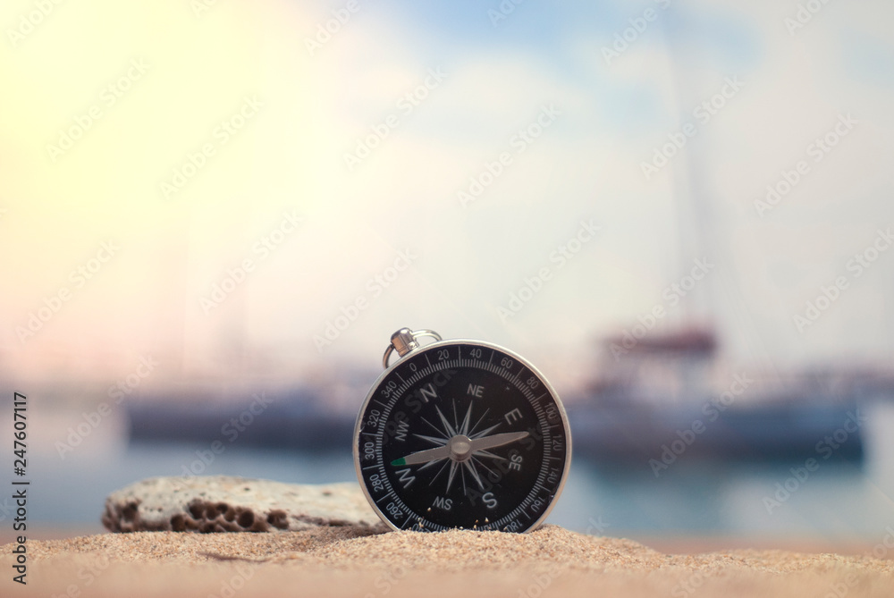 Time to travel. An idea for tourism with a compass in the sand with corals in the background of the sea and a parking for yachts. - obrazy, fototapety, plakaty 