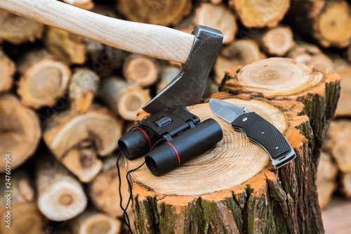 axe, binoculars and jackknife case on the stump, firewoods on the background photo