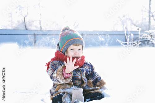 baby in winter clothes outdoor remove her mittens and say hello. cute child in cap,scarf and mittens among the snow