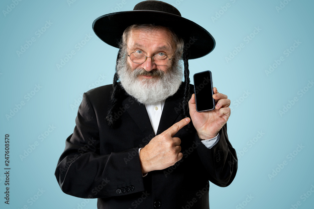 Portrait of old senior orthodox Hasdim Jewish man with mobile phone at Jewish festival of Purim at studio. The purim, jewish, festival, holiday, celebration, judaism, tradition, business Portrait of old senior orthodox Hasdim Jewish man with mobile phone at Jewish festival of Purim at studio. The purim, jewish, festival, holiday, celebration, judaism, tradition, business