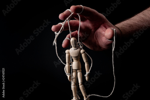 Employer manipulating the employee, emotional manipulation and obey the master concept with ominous hand pulling the strings on a marionette with moody contrast on black background photo