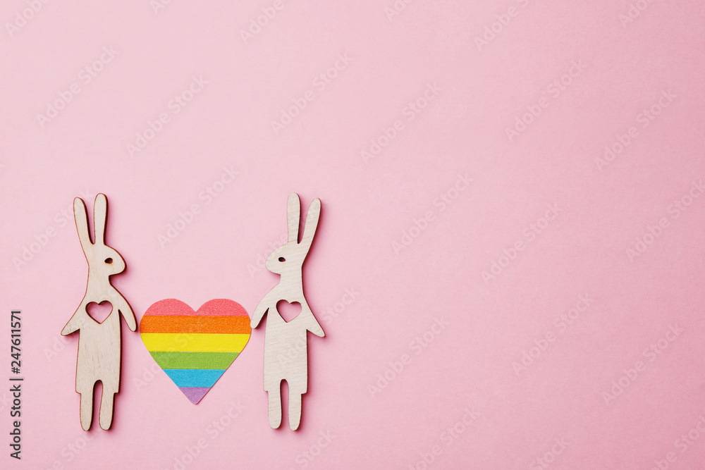 rainbow LGBT heart and wooden rabbits on pink background, copy space