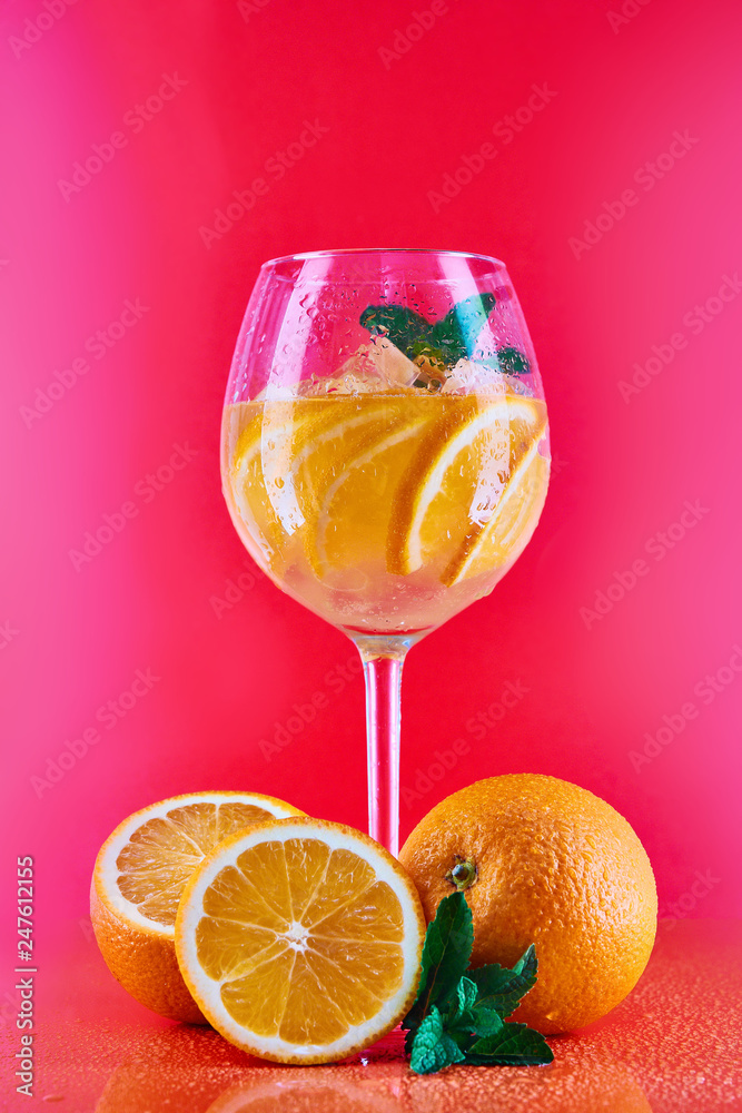 orange cocktail in a wine glass with mint on a red, coral background with oranges
