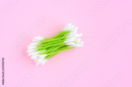 Individual ear sticks with green plastic pick and cotton buds with selective focus on pink background. Clean ear swabs for personal ears hygiene. Sterile softness applicator for cleanliness earwax 