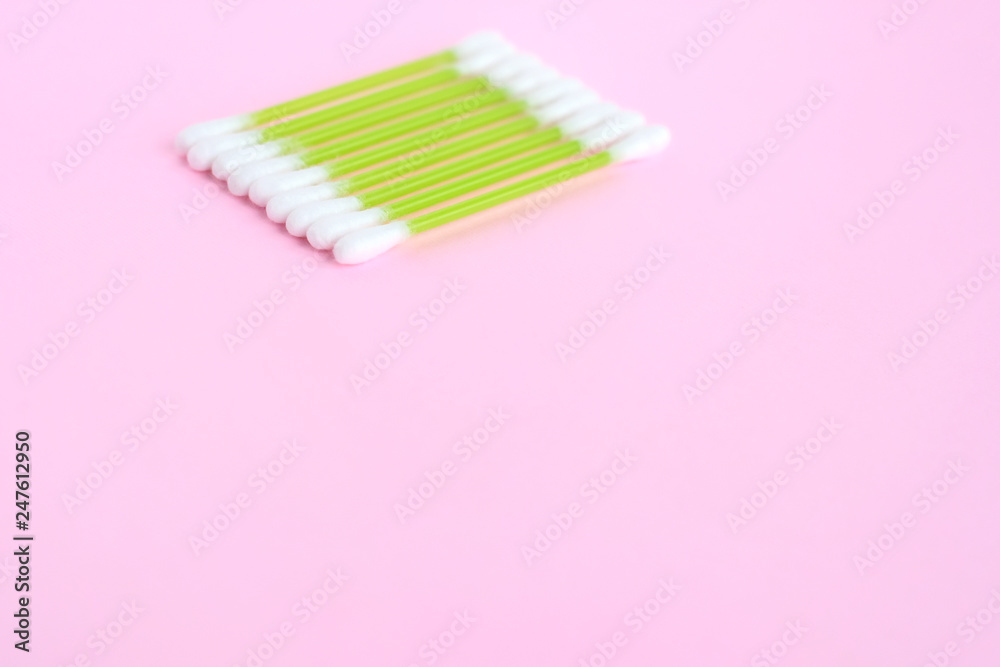 Individual ear sticks with green plastic pick and cotton buds with selective focus on pink background. Clean ear swabs for personal ears hygiene. Sterile softness applicator for cleanliness earwax Individual ear sticks with green plastic pick and cotton buds with selective focus on pink background. Clean ear swabs for personal ears hygiene. Sterile softness applicator for cleanliness earwax