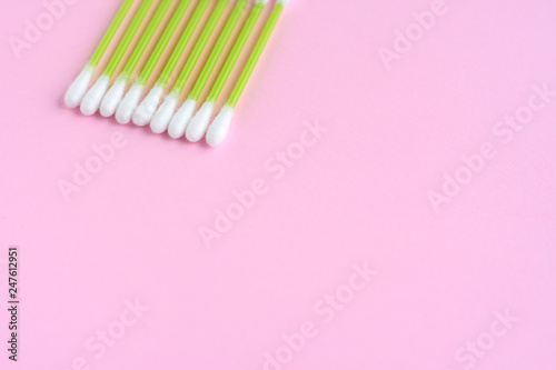 Individual ear sticks with green plastic pick and cotton buds with selective focus on pink background. Clean ear swabs for personal ears hygiene. Sterile softness applicator for cleanliness earwax 