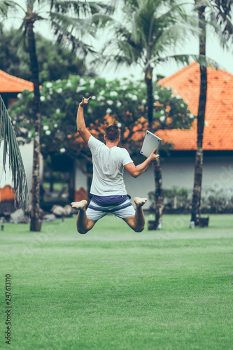 Young freelancer man jumping with laptop in the tropical park of Bali island. © belart84