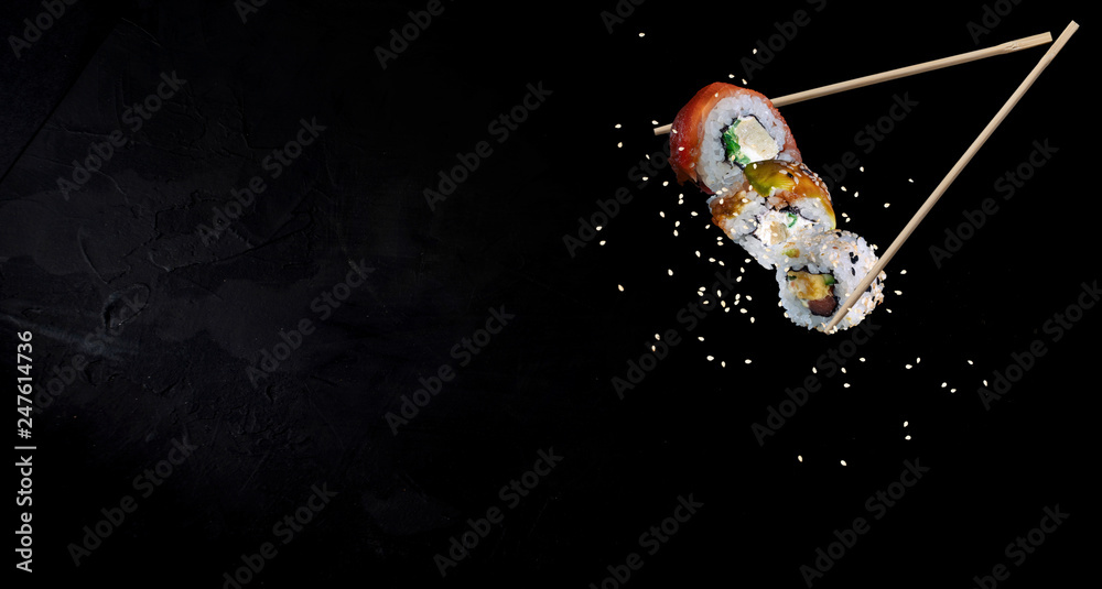 Εκτύπωση καμβά Sushi pieces placed between chopsticks, separated on black background