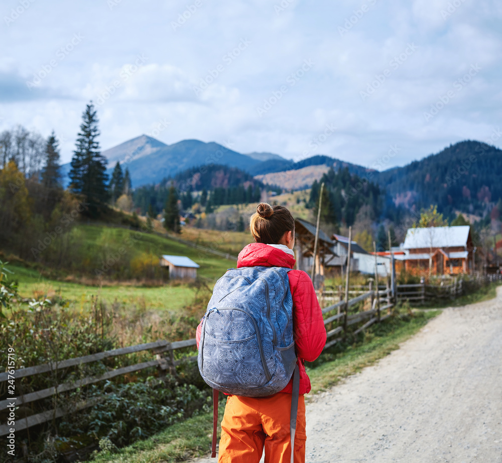 Naklejka premium woman hiker with backpack, wearing in red jacket and orange pants, standing on the mountains background