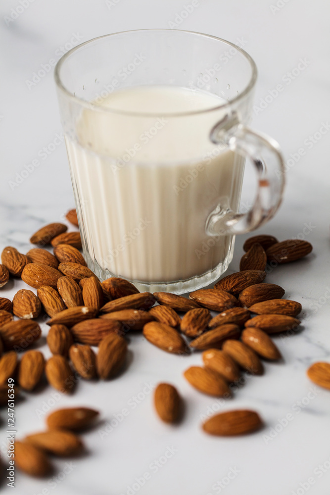 Fototapeta premium Almond milk in a glass surrounded by organic almonds