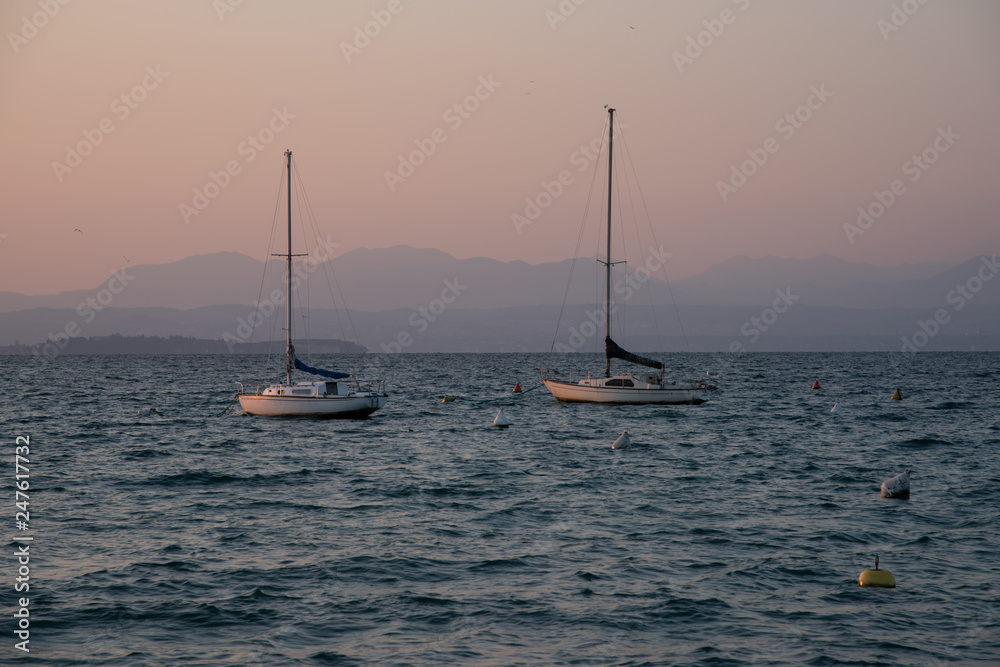 Two sailboats moored in the middle of the lake on a winter afternoon. Warm and afternoon light. Profile of mountains in the background.