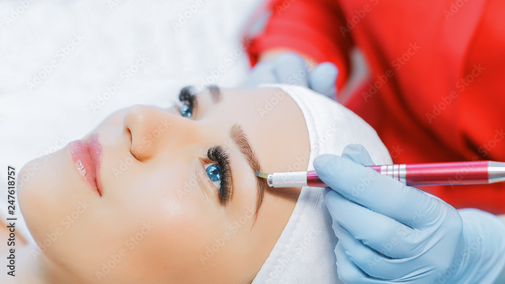 Eyelash Extension Procedure. Woman Eye with Long Eyelashes. Beautiful young girl  tweezing her eyebrows in a beauty salon. Eyebrow Correction. Beauty Concept. Permanent Makeup. Microblading brow.