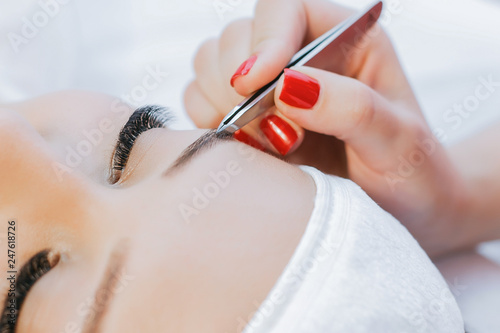 Eyelash Extension Procedure. Woman Eye with Long Eyelashes. Beautiful young girl tweezing her eyebrows in a beauty salon. Eyebrow Correction. Beauty Concept. Permanent Makeup. Microblading brow.