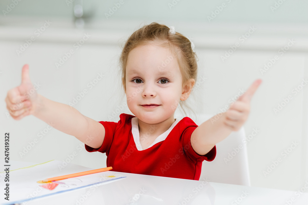 Cute smart little caucasian girl in casual red dress is happy and shows thumb up Cute smart little caucasian girl in casual red dress is happy and shows thumb up