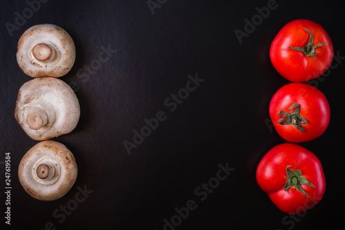 Mushrooms champignons with red tomatoes on a black background