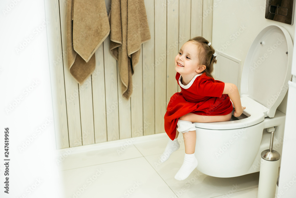 Cute clever little caucasian girl in everyday red dress is sitting on the  toilet and laughing. Teaching a child to go to the toilet as adults Photos  | Adobe Stock