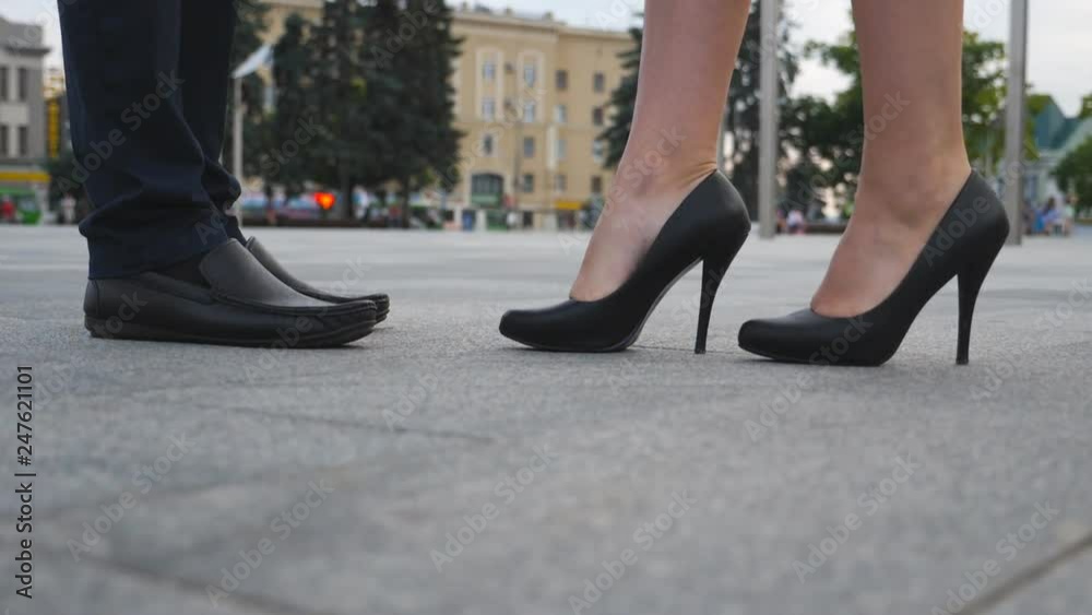 Feet of businessman in black shoes and businesswoman on high heels standing at city street. Business meeting between business partners outdoor. Low angle view Close up Slow motion Feet of businessman in black shoes and businesswoman on high heels standing at city street. Business meeting between business partners outdoor. Low angle view Close up Slow motion