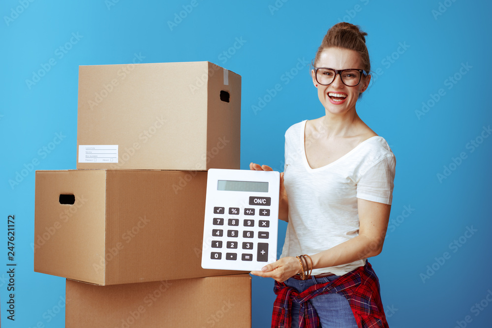 smiling woman near cardboard box showing calculator on blue smiling woman near cardboard box showing calculator on blue
