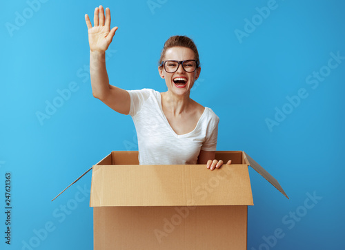 happy young woman get out of cardboard box and on blue