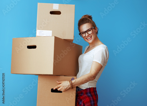 smiling young woman holding pile of cardboard boxes on blue