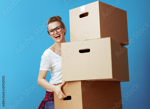 happy young woman holding pile of cardboard boxes on blue