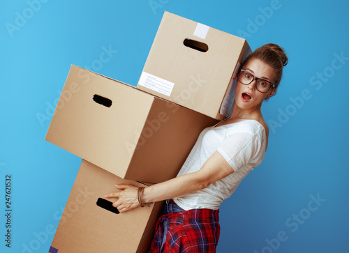 shocked modern woman holding pile of cardboard boxes on blue