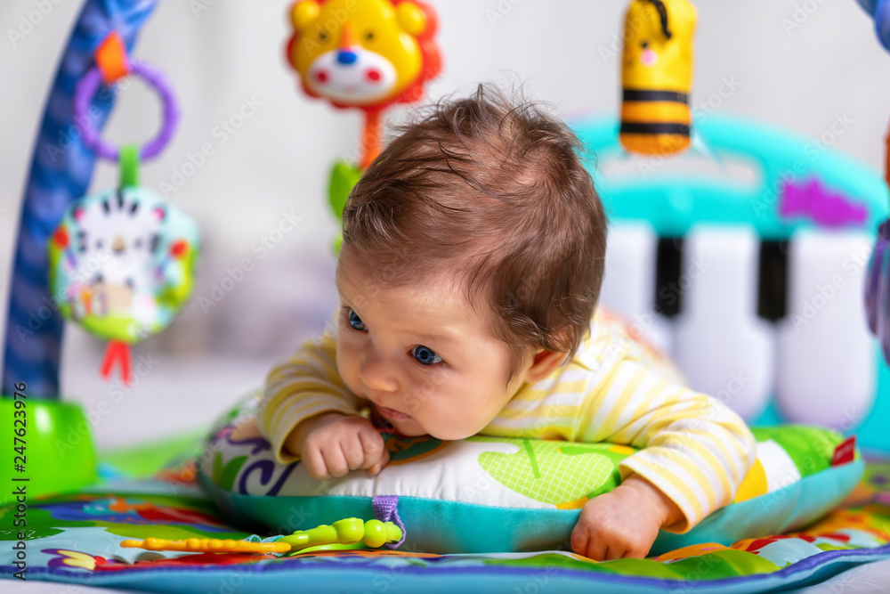 Fototapeta premium Neugeborenes Baby mit bunten Spielsachen liegt auf den Bauch