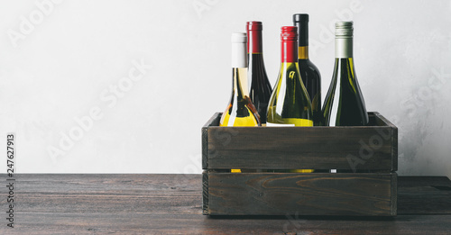 Set of different kinds bottles of champagne, white, red wine in wooden box on light background