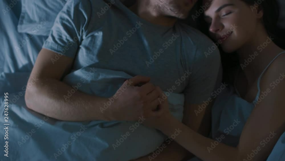 Top View Bed at Night: Attractive young Couple Sleeping Together, Holding Each other in Arms, Embracing. First Rays of Morning Sun Illuminate Room Trough the Window Top View Bed at Night: Attractive young Couple Sleeping Together, Holding Each other in Arms, Embracing. First Rays of Morning Sun Illuminate Room Trough the Window