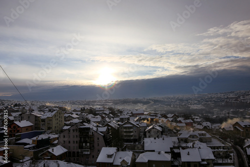 Beautiful view of winter morning fog, snow and sun filling on landscape of houses and buildings in Belgrade. Scenery during sunrise, sunset of top view at settlement is very popular for photographer.