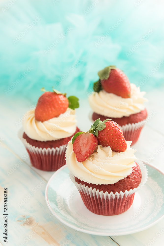 Three cupcake red velvet with a cap of cream cheese and strawberries on a blue background Three cupcake red velvet with a cap of cream cheese and strawberries on a blue background