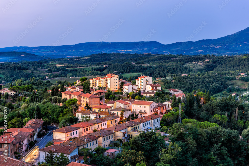 Chiusi village cityscape at night before sunrise in Umbria Italy with illuminated lights and rooftop houses on mountain countryside and rolling hills