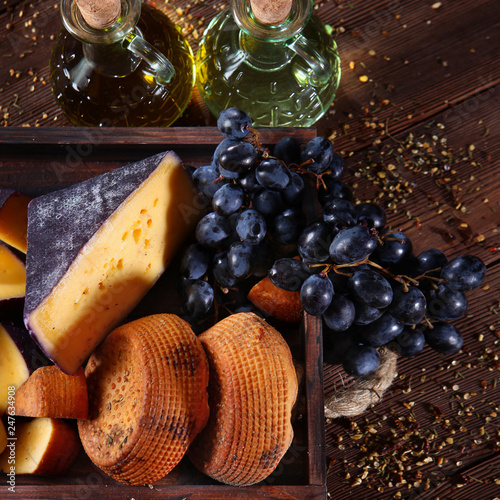 Cheeses and grapes in wooden box on wooden background. The view from the top. A pair of glass bottles of olive oil. Blank space for label or label. The concept of still life.