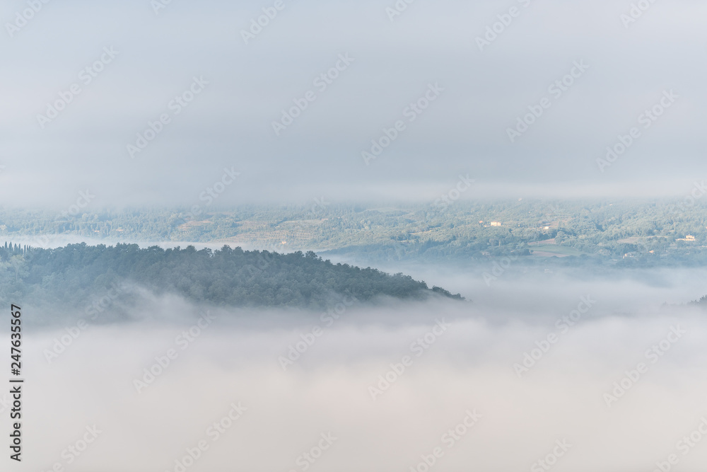 Chiusi Scalo mountain mist fog sunrise and villas houses in Umbria and Tuscany in Italy with soft clouds covering blanketing inversion in summer