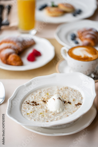 Bowl of breakfast oatmeal with soft Italian cheese and cinnamon. Croissants, coffee and other dishes on the table in the restaurant