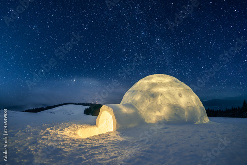 Fantastic winter landscape glowing by star light. Wintry scene with snowy igloo and milky way in night sky © Ivan Kmit