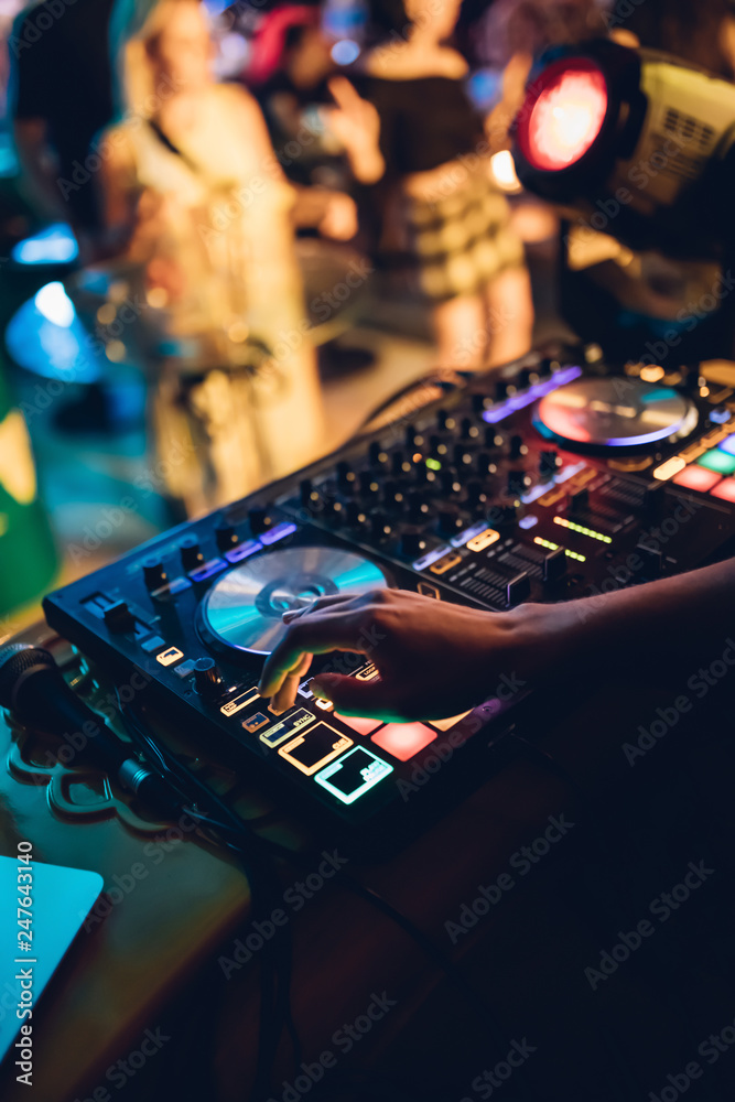 Naklejka premium DJ plays live set and mixing music on turntable console at stage in the night club. Disc Jokey Hands on a sound mixer station at club party. DJ mixer controller panel for playing music and partying.