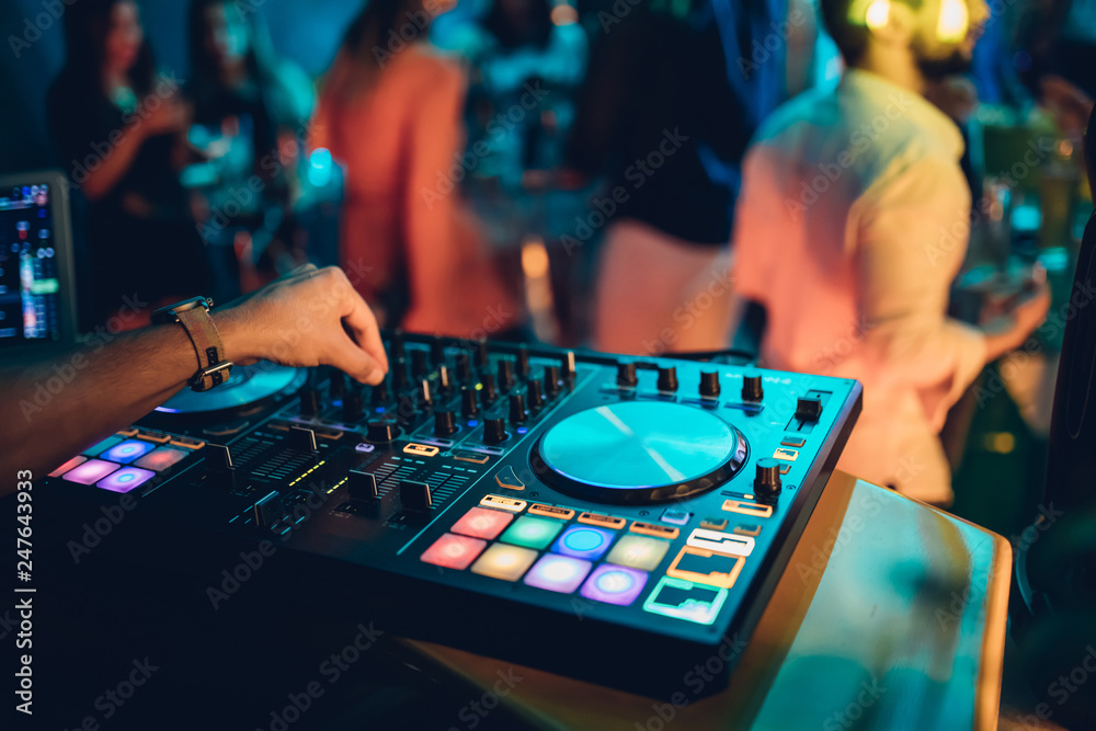 Fototapeta premium DJ plays live set and mixing music on turntable console at stage in the night club. Disc Jokey Hands on a sound mixer station at club party. DJ mixer controller panel for playing music and partying.