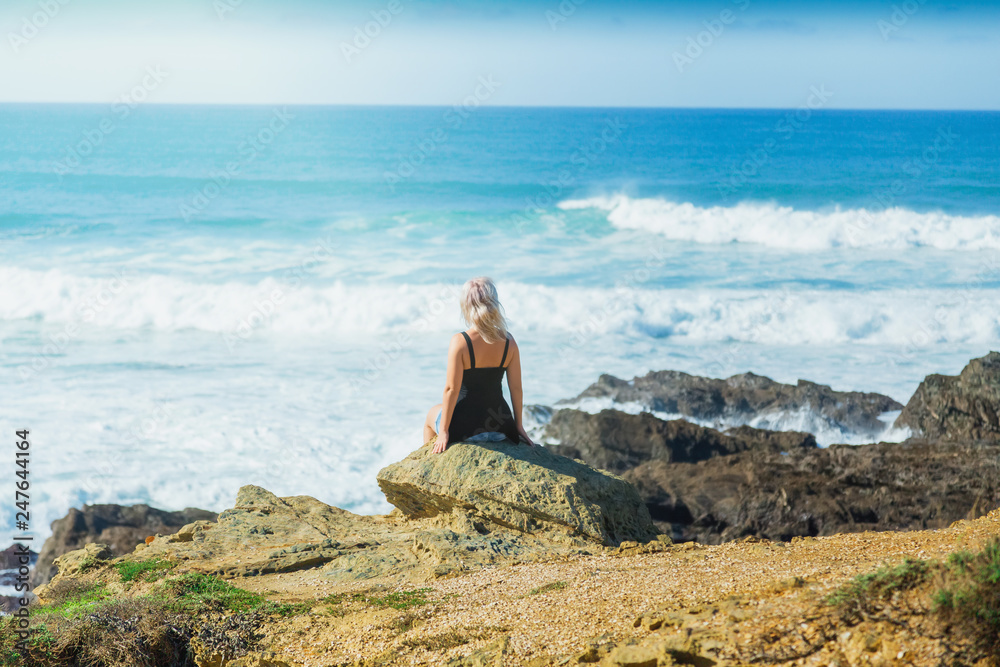 Girl sitting on the rocks and looks at ocean