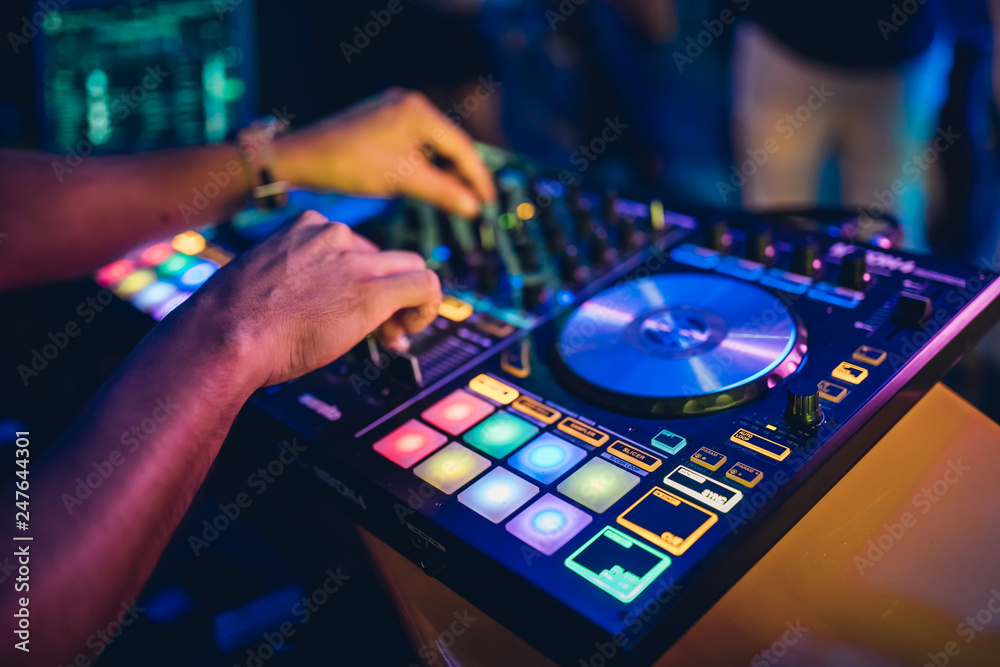 DJ plays live set and mixing music on turntable console at stage in the night club. Disc Jokey Hands on a sound mixer station at club party. DJ mixer controller panel for playing music and partying. DJ plays live set and mixing music on turntable console at stage in the night club. Disc Jokey Hands on a sound mixer station at club party. DJ mixer controller panel for playing music and partying.