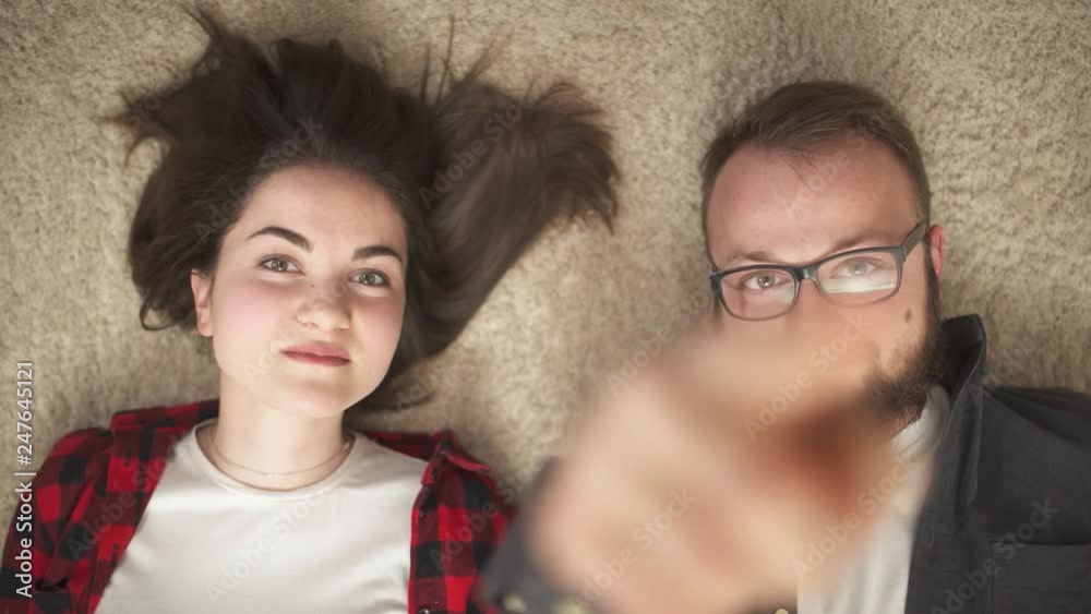 A top view of a happy young couple lying on the floor, looking at the camera and smiling