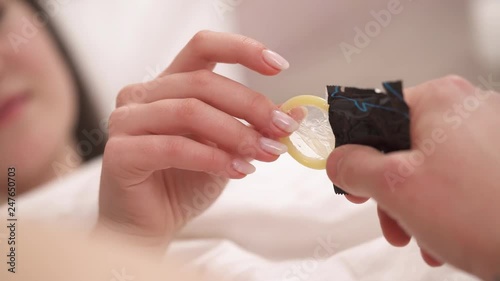 Close-up of the hand of a girl pulling out a condom. Loving couple lying on the bed under the blanket. photo