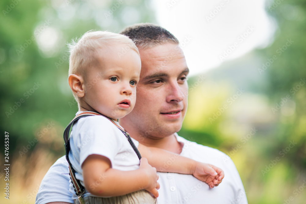 Young father holding a small toddler son in sunny summer nature. Young father holding a small toddler son in sunny summer nature.